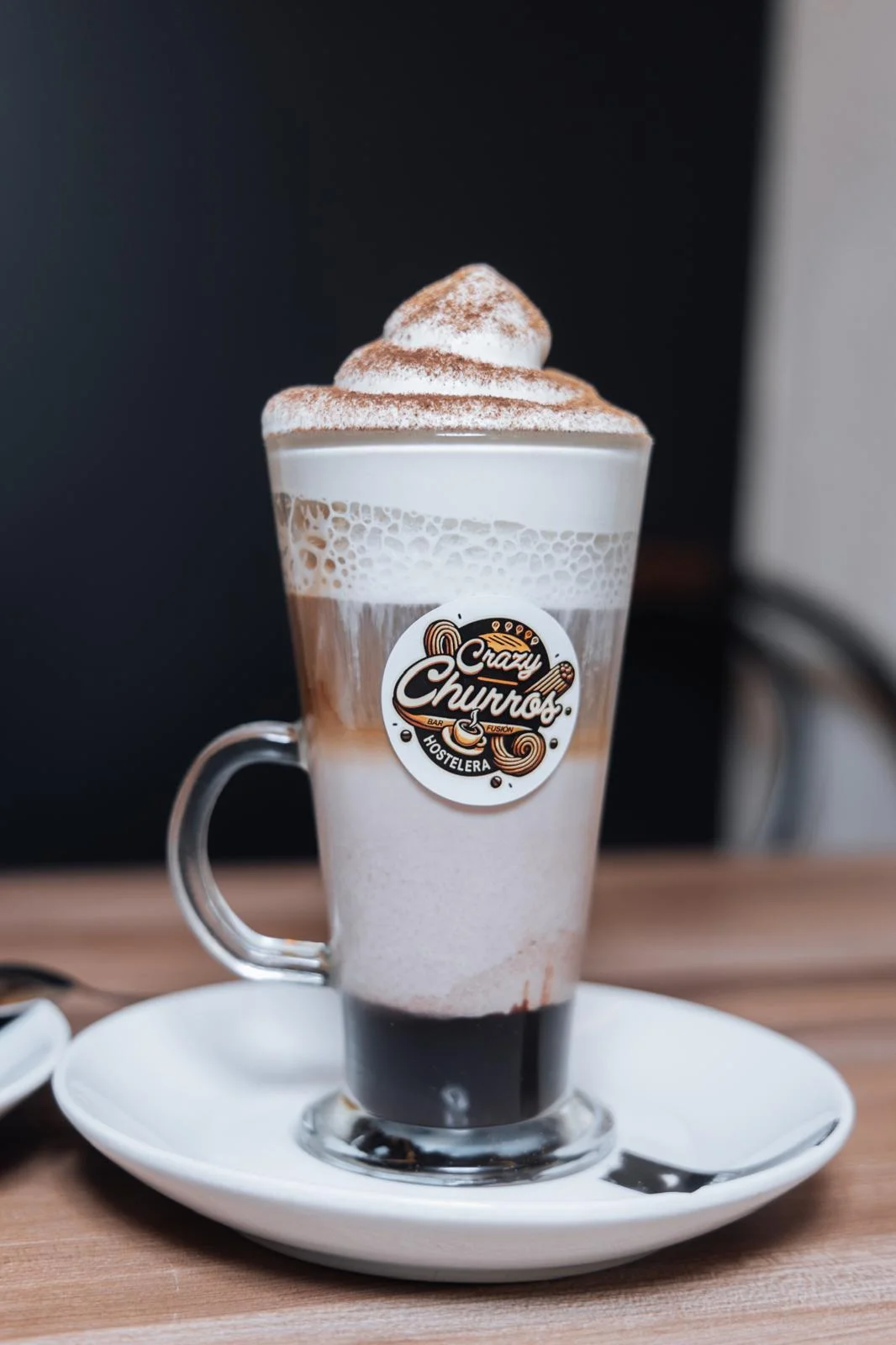 Café latte en vaso alto con nata, canela y la pegatina de Crazy Churros